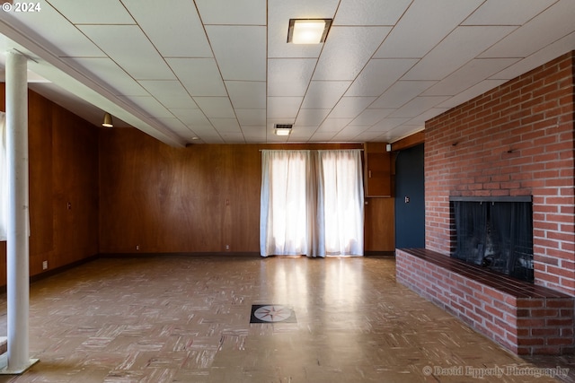 unfurnished living room featuring a brick fireplace, wooden walls, and parquet floors