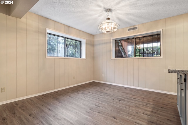 unfurnished room featuring dark wood-type flooring, a notable chandelier, a textured ceiling, and wood walls