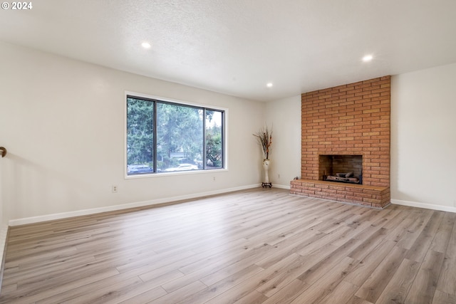 unfurnished living room with a textured ceiling, a brick fireplace, and light wood-type flooring