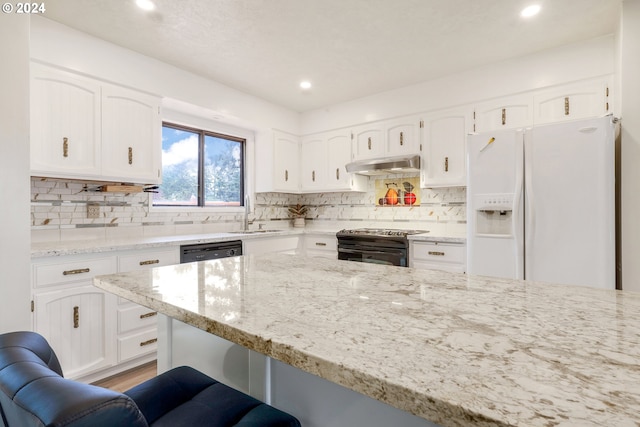 kitchen featuring black range with electric stovetop, white cabinetry, a kitchen bar, light stone counters, and white refrigerator with ice dispenser