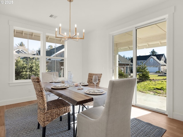 dining space featuring a notable chandelier, wood-type flooring, and a healthy amount of sunlight