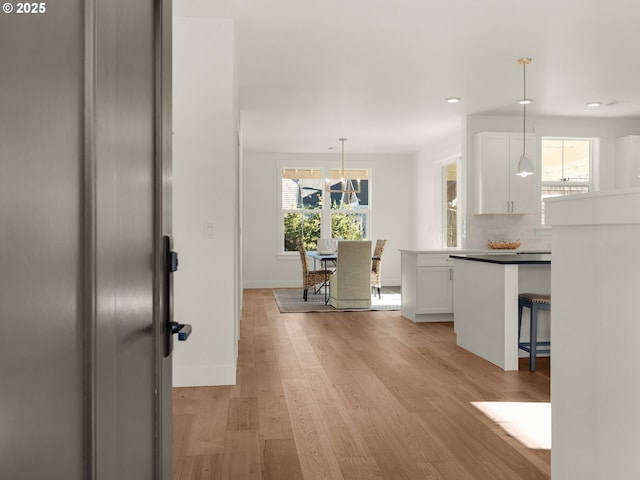 kitchen with white cabinetry, tasteful backsplash, hanging light fixtures, light hardwood / wood-style flooring, and a kitchen breakfast bar