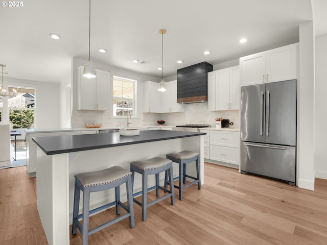 kitchen with stainless steel fridge, premium range hood, white cabinetry, decorative light fixtures, and light wood-type flooring