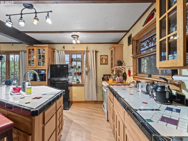 kitchen with tile counters, stainless steel fridge, light wood-type flooring, and an island with sink