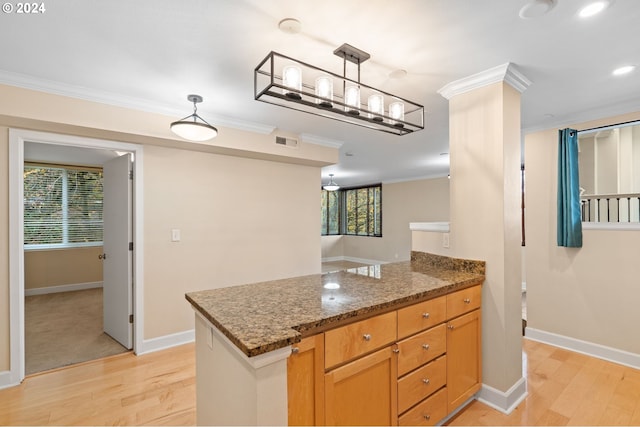 kitchen with dark stone counters, crown molding, hanging light fixtures, a wealth of natural light, and light hardwood / wood-style floors