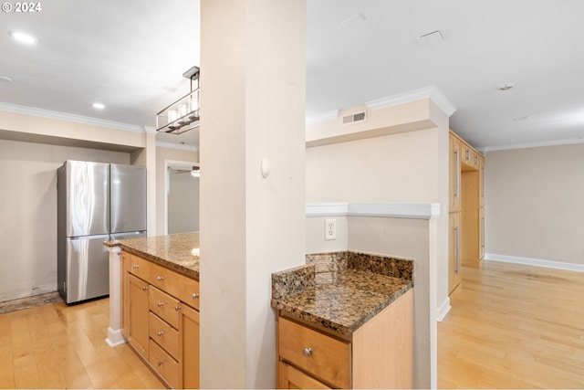 kitchen featuring crown molding, light hardwood / wood-style flooring, stainless steel refrigerator, and dark stone counters