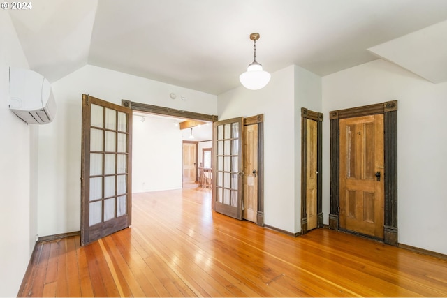 spare room featuring a wall mounted air conditioner, vaulted ceiling, wood-type flooring, and french doors