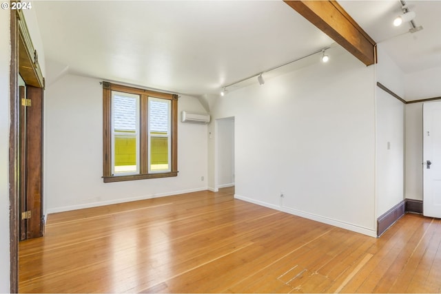 empty room featuring a wall mounted AC, light hardwood / wood-style flooring, lofted ceiling with beams, and track lighting