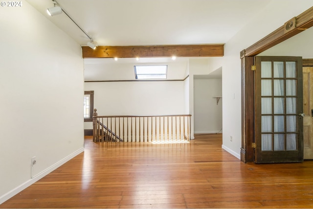 spare room with beamed ceiling, hardwood / wood-style floors, and track lighting