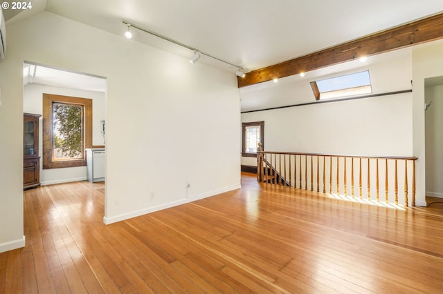 empty room with light hardwood / wood-style floors, track lighting, plenty of natural light, and lofted ceiling with skylight