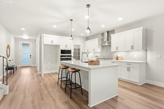 kitchen featuring white cabinetry, a center island with sink, appliances with stainless steel finishes, wall chimney range hood, and pendant lighting