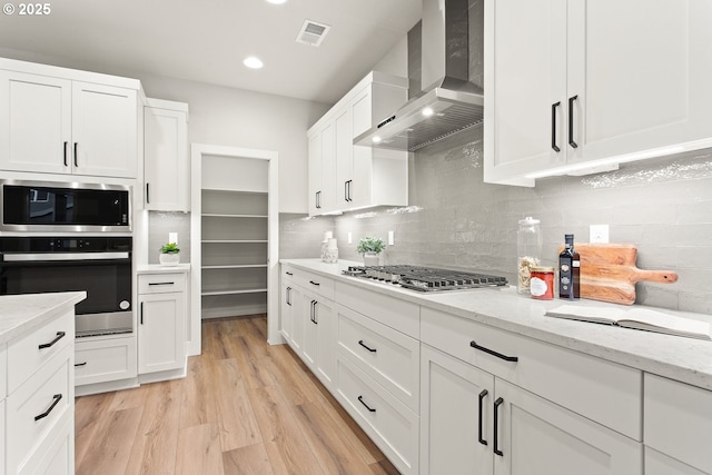 kitchen with light stone countertops, white cabinets, and wall chimney exhaust hood