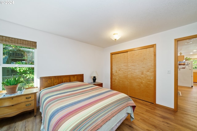 bedroom with white refrigerator, light hardwood / wood-style floors, and a closet