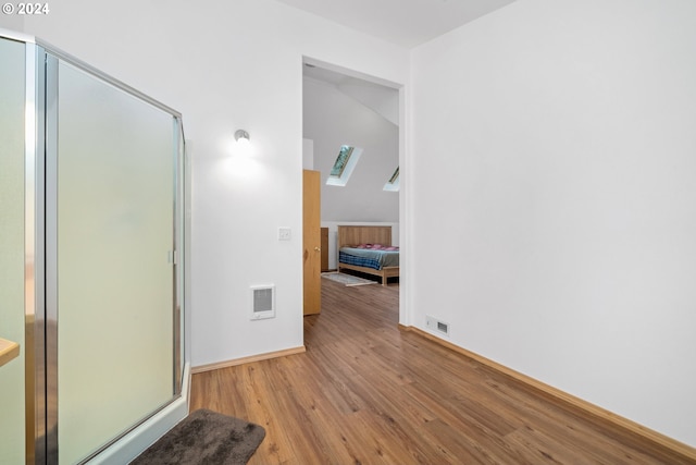 bathroom with hardwood / wood-style flooring, a shower with door, and a skylight