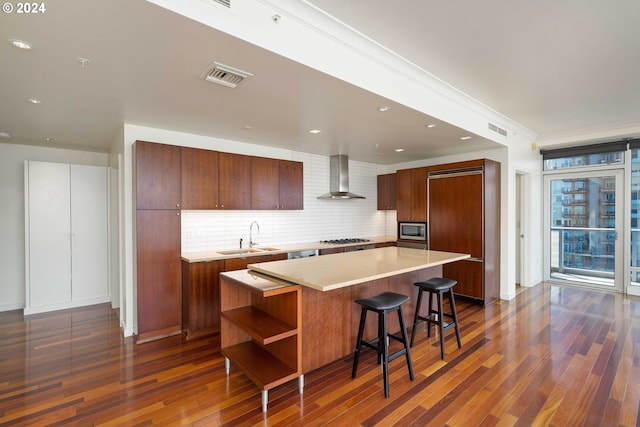 kitchen with a kitchen bar, sink, a kitchen island, stainless steel appliances, and wall chimney range hood