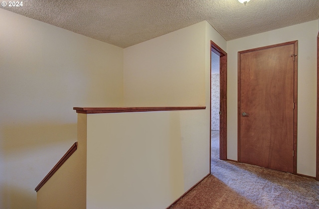 hall with a textured ceiling and light colored carpet