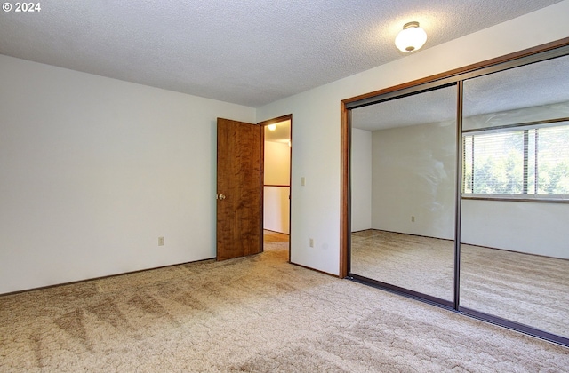 unfurnished bedroom with a textured ceiling, light colored carpet, and a closet