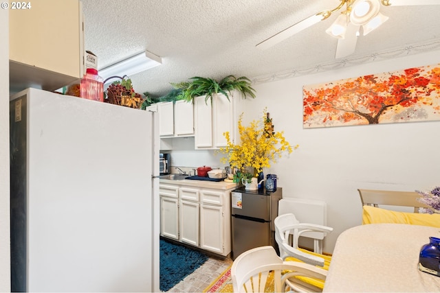 kitchen featuring a textured ceiling, ceiling fan, white fridge, and white cabinets