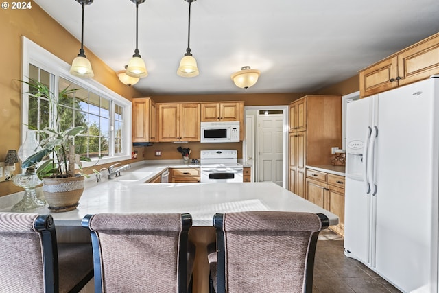 kitchen with a breakfast bar area, white appliances, dark tile floors, and decorative light fixtures