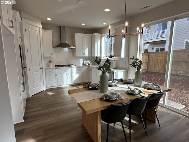 kitchen featuring dark hardwood / wood-style flooring, decorative light fixtures, white cabinetry, and wall chimney range hood