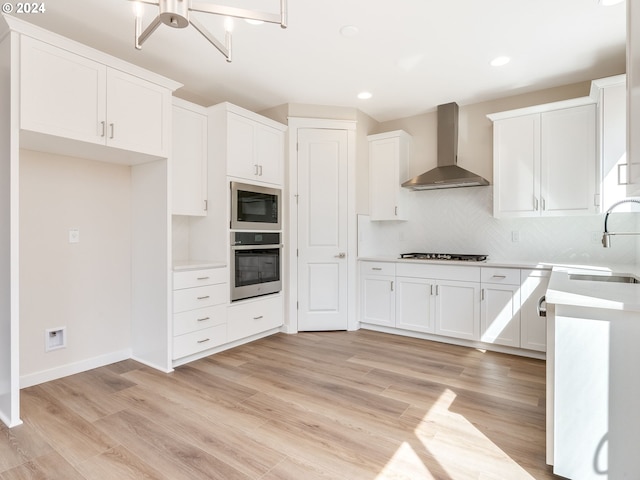 kitchen featuring appliances with stainless steel finishes, sink, white cabinetry, and wall chimney range hood