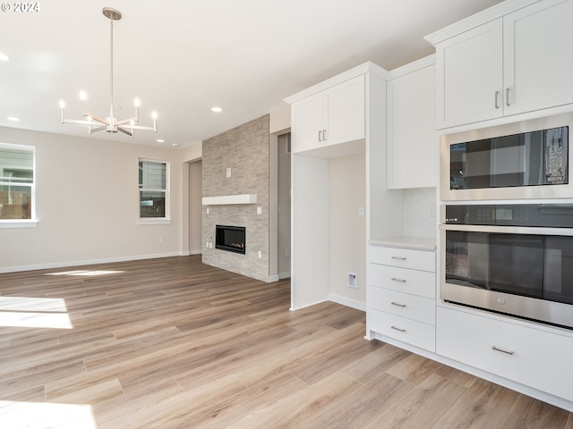 kitchen featuring stainless steel oven, built in microwave, light hardwood / wood-style floors, white cabinetry, and a stone fireplace