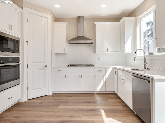 kitchen with appliances with stainless steel finishes, white cabinetry, and wall chimney range hood