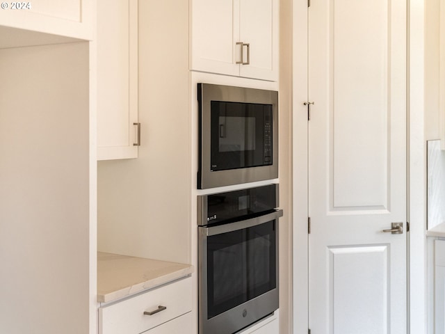 kitchen with stainless steel oven, light stone counters, white cabinetry, and built in microwave