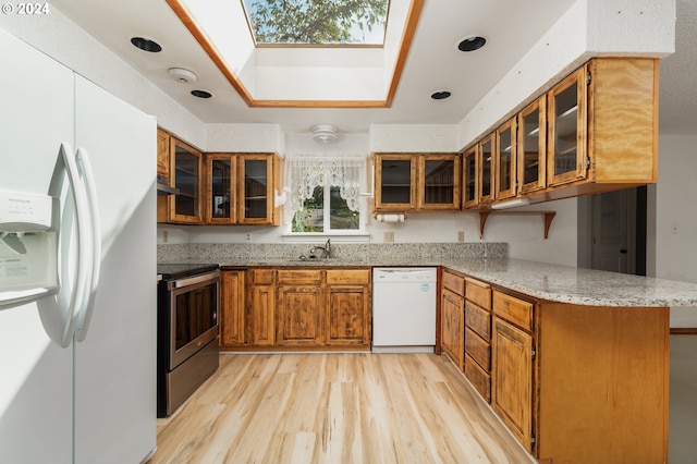 kitchen featuring white appliances, kitchen peninsula, light hardwood / wood-style flooring, a skylight, and sink