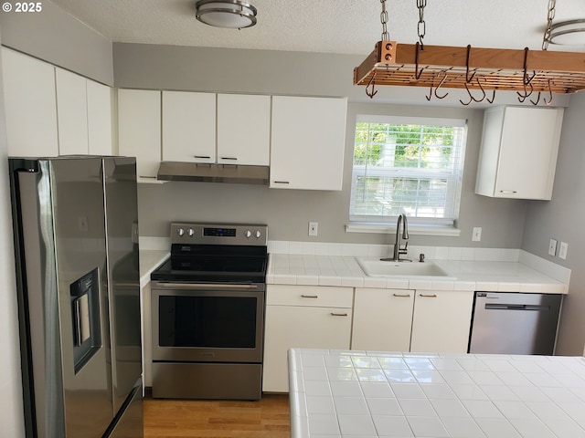 8550 SW Curry Dr Unit A, Wilsonville, OR 97070 - kitchen with appliances with stainless steel finishes, under cabinet range hood, a sink, tile countertops, and white cabinets