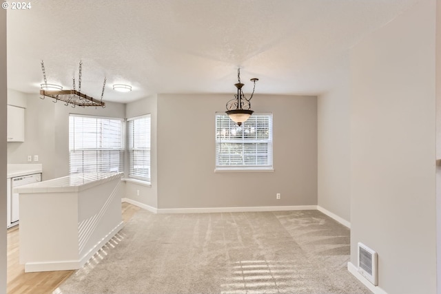 unfurnished dining area featuring a textured ceiling and light colored carpet