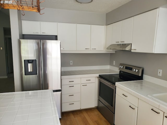 8550 SW Curry Dr Unit A, Wilsonville, OR 97070 - kitchen with stainless steel appliances, under cabinet range hood, tile counters, and white cabinetry