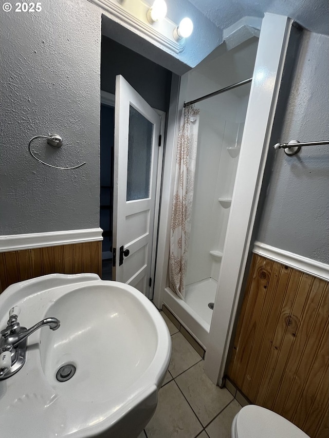 bathroom featuring a textured wall, a sink, wainscoting, a shower stall, and tile patterned floors