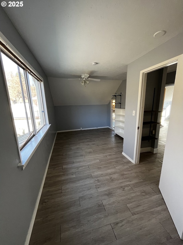 empty room featuring lofted ceiling, ceiling fan, baseboards, and dark wood-type flooring