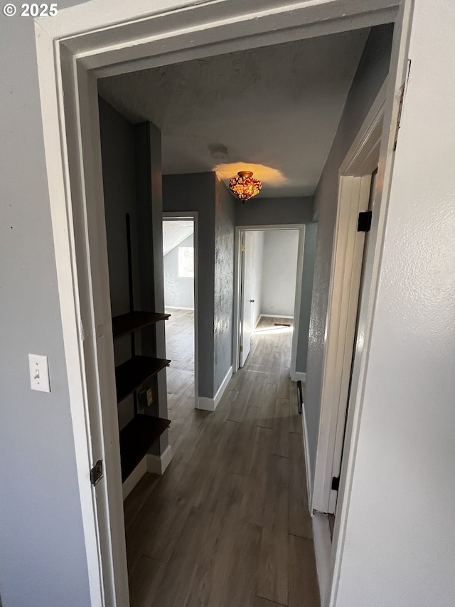 hall with a textured wall, dark wood finished floors, and baseboards