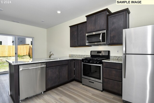 kitchen featuring sink, light hardwood / wood-style floors, kitchen peninsula, stainless steel appliances, and light stone countertops