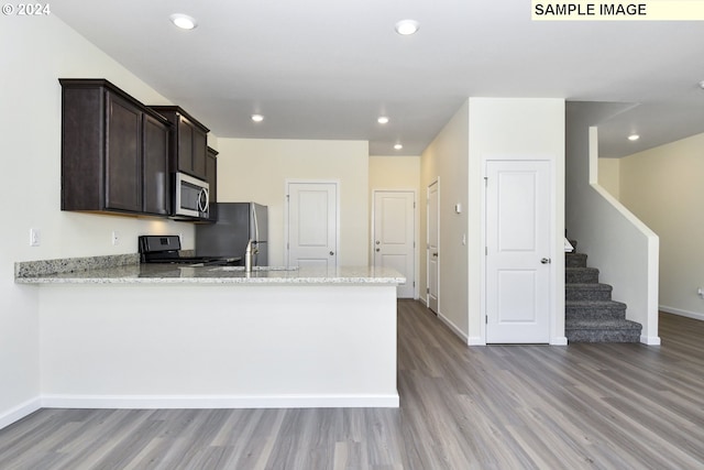 kitchen with light stone counters, light hardwood / wood-style flooring, kitchen peninsula, and appliances with stainless steel finishes