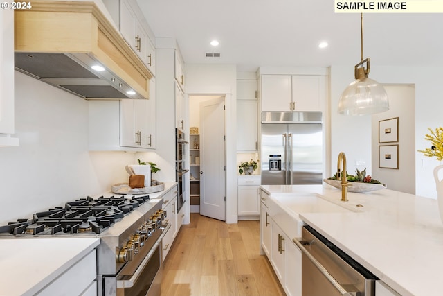 kitchen featuring premium appliances, light wood-style flooring, premium range hood, white cabinets, and light countertops