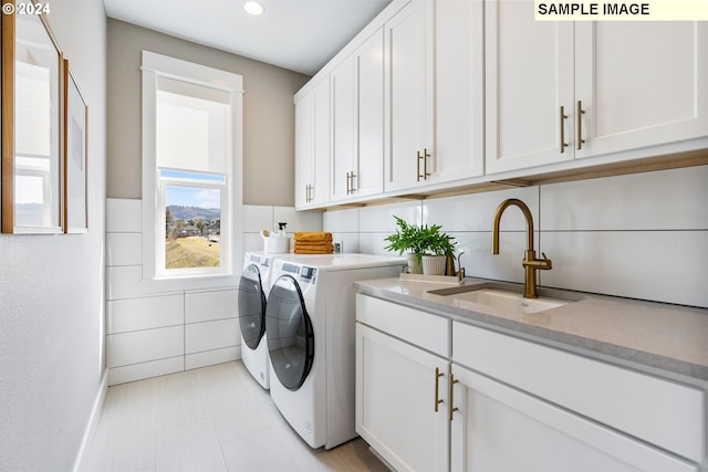 clothes washing area featuring cabinets, sink, washing machine and dryer, and tile walls