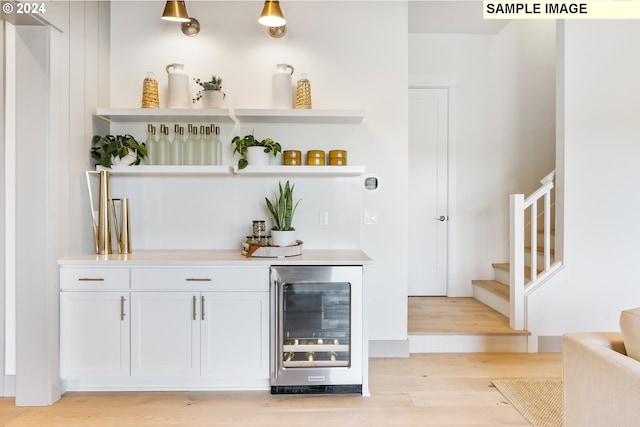 bar featuring stairway, beverage cooler, a bar, and light wood finished floors