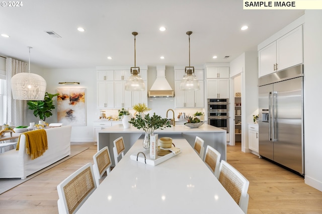 kitchen with light wood finished floors, custom exhaust hood, visible vents, light countertops, and appliances with stainless steel finishes