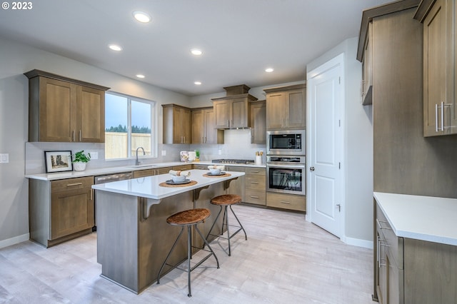 kitchen with sink, a kitchen island, stainless steel appliances, light hardwood / wood-style floors, and a kitchen bar