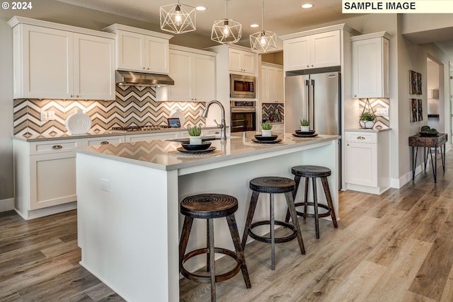 kitchen featuring hanging light fixtures, a kitchen island with sink, white cabinetry, appliances with stainless steel finishes, and light hardwood / wood-style floors