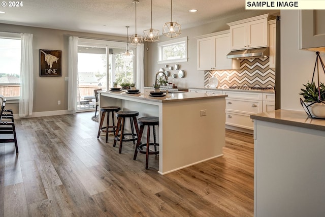 kitchen featuring white cabinets, a kitchen island with sink, pendant lighting, and plenty of natural light