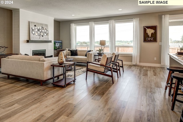 living room featuring light hardwood / wood-style floors, a textured ceiling, a fireplace, and a wealth of natural light