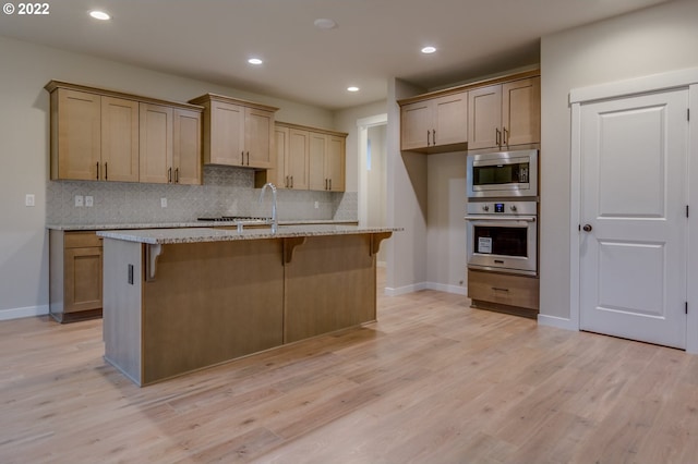 kitchen with a kitchen island with sink, light stone countertops, light hardwood / wood-style floors, a kitchen bar, and stainless steel appliances