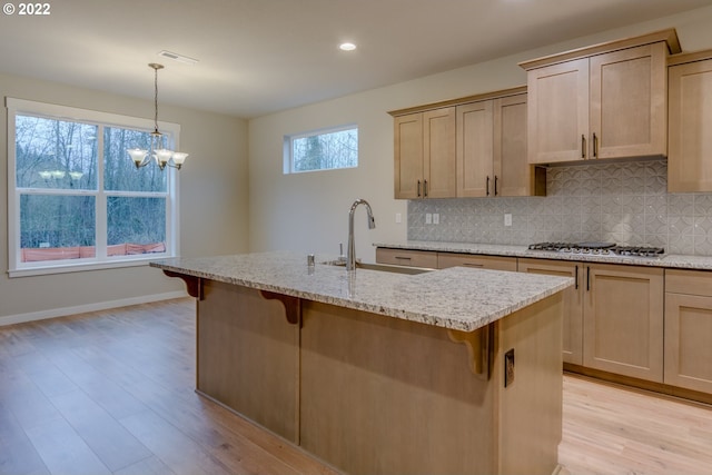 kitchen with a kitchen bar, light brown cabinetry, pendant lighting, and stainless steel gas cooktop