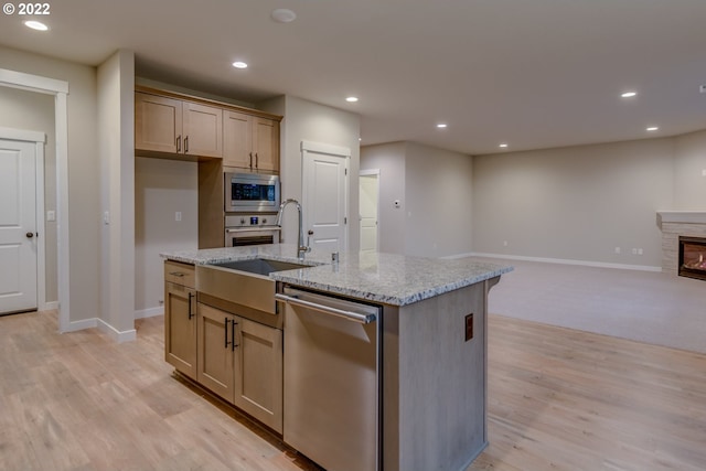 kitchen with a stone fireplace, light stone counters, a center island with sink, and appliances with stainless steel finishes