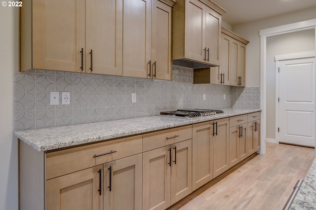 kitchen with decorative backsplash, light stone countertops, light brown cabinetry, light hardwood / wood-style floors, and stainless steel gas cooktop