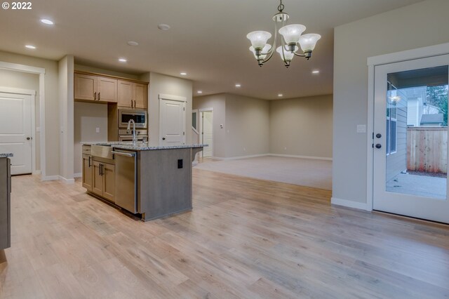 kitchen with pendant lighting, an island with sink, a notable chandelier, light stone counters, and stainless steel appliances